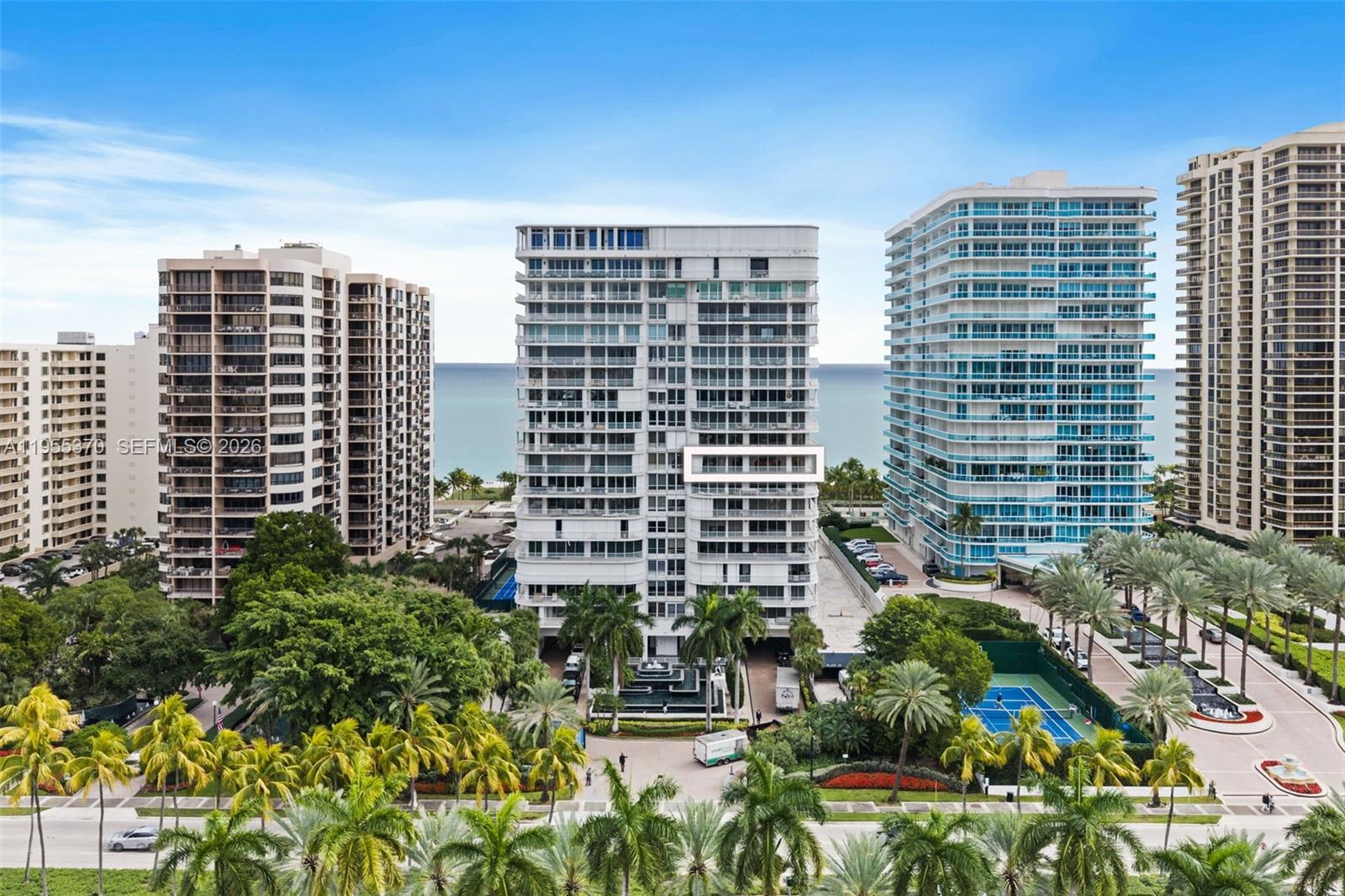 An exterior view of a tall residential building surrounded by palm trees and a tennis court — 10155 Collins Ave # 909, Bal Harbour FL 33154, BAL HARBOUR, FL