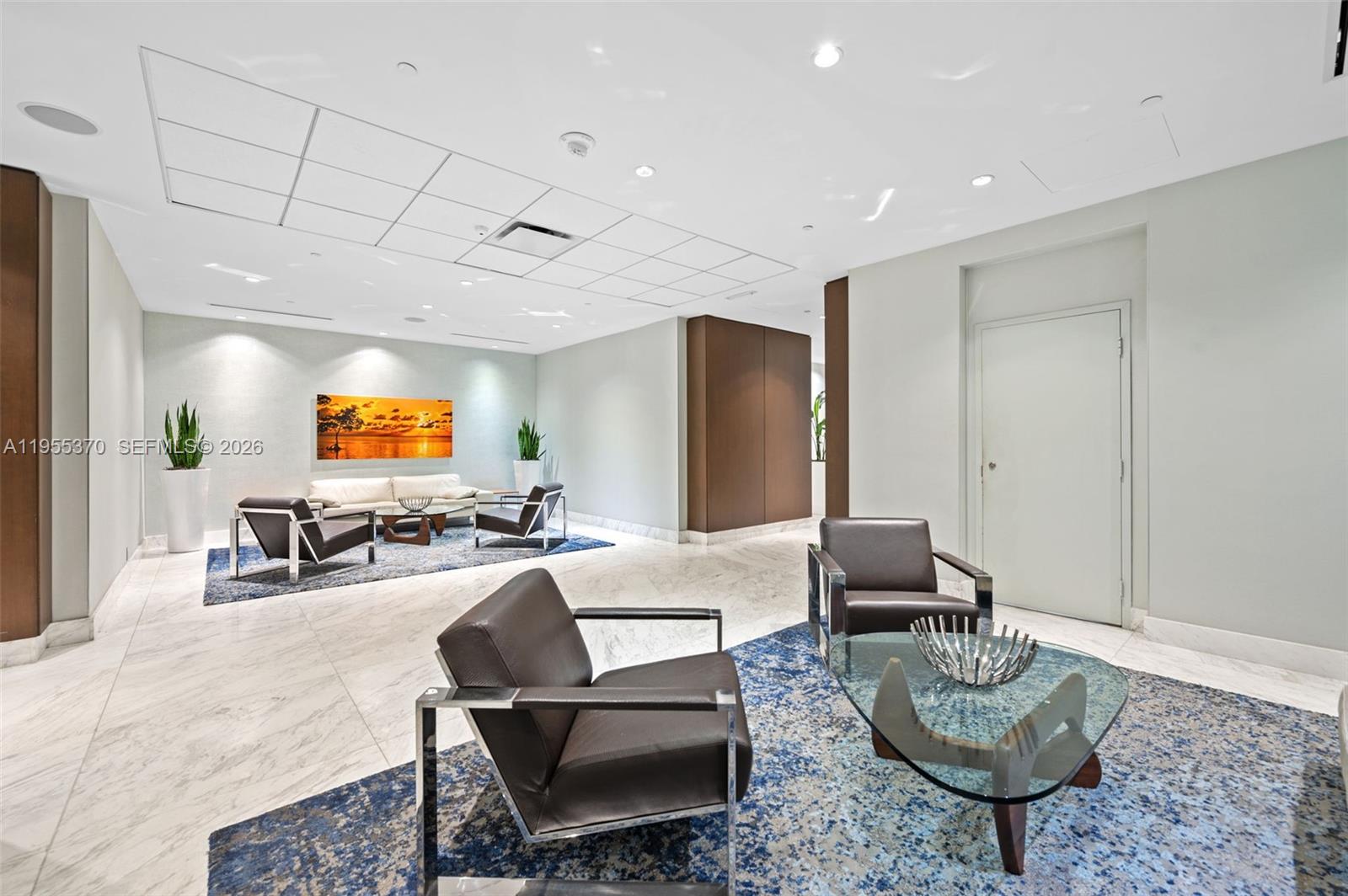 A modern lobby features marble floors, two seating areas with dark leather chairs, and recessed lighting — 10155 Collins Ave # 909, Bal Harbour FL 33154, BAL HARBOUR, FL