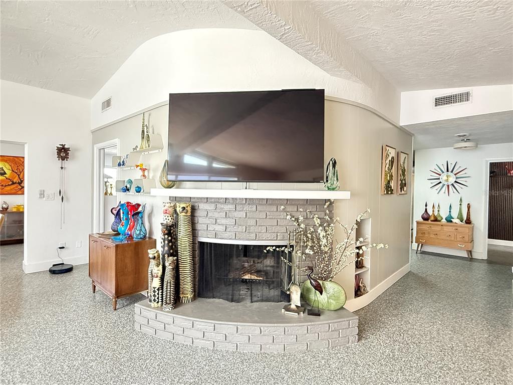 A living room features a curved gray brick fireplace with a mounted television above it — 801 FAIRWAY DRIVE, NEW SMYRNA BEACH, FL