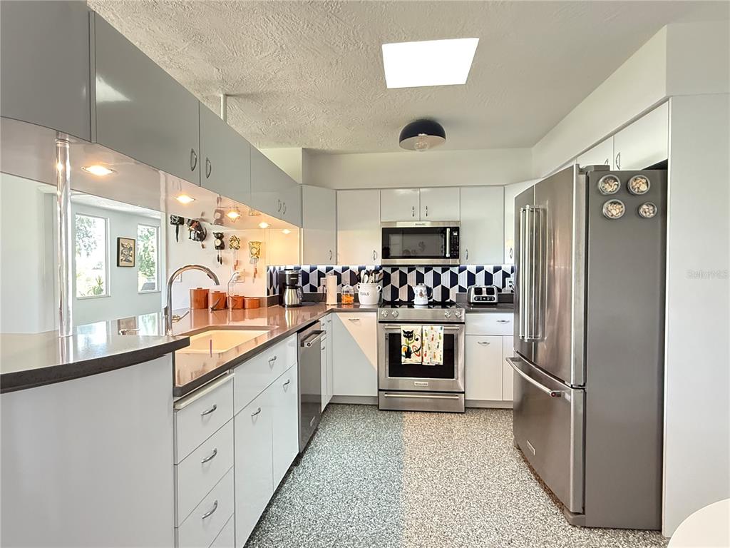 A kitchen features gray cabinets, stainless steel appliances, and a black and white tiled backsplash — 801 FAIRWAY DRIVE, NEW SMYRNA BEACH, FL