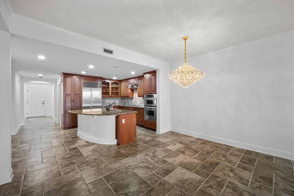 A kitchen with dark wood cabinets, granite countertops, and a crystal chandelier over tile flooring — 146 PALM COAST RESORT BOULEVARD UNIT 509, PALM COAST, FL