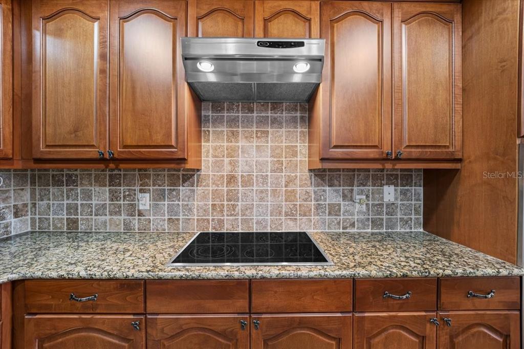 A kitchen features wood cabinets, a granite countertop, a glass cooktop, and a tiled backsplash — 146 PALM COAST RESORT BOULEVARD UNIT 509, PALM COAST, FL