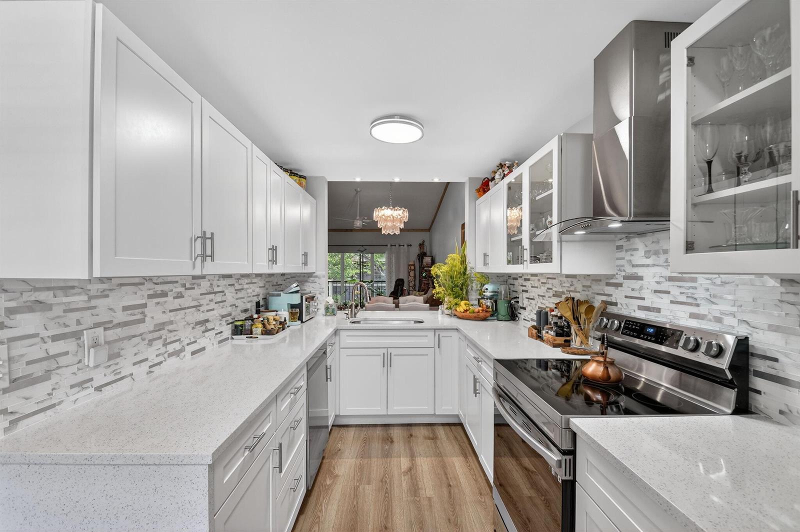 A galley kitchen features white cabinets, quartz countertops, stainless steel appliances, and a tiled backsplash — 7855 Willow Spring Drive # 725, Lake Worth FL 33467, LAKE WORTH, FL