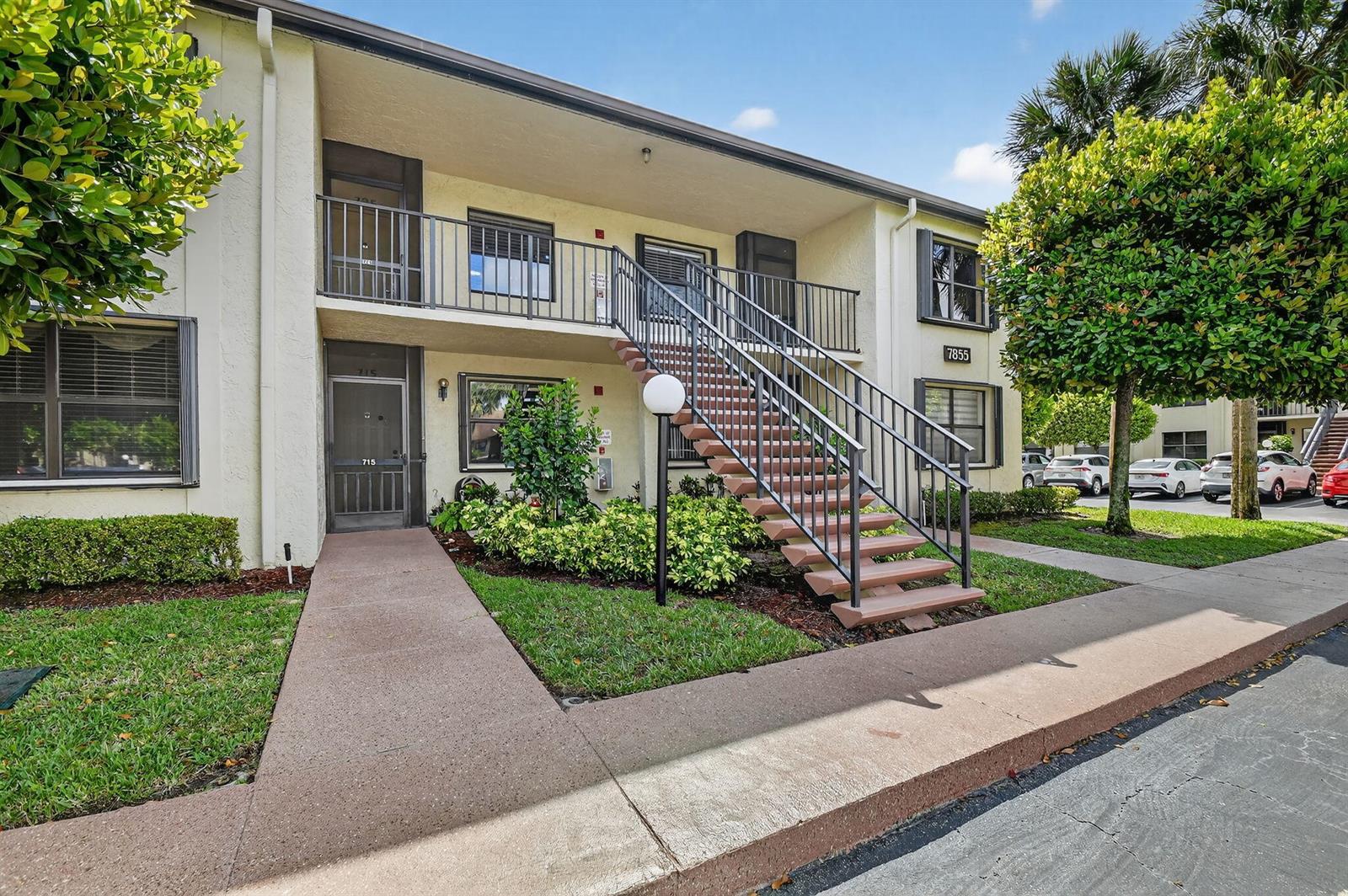 A two-story apartment building exterior features a central staircase leading to an upper balcony — 7855 Willow Spring Drive # 725, Lake Worth FL 33467, LAKE WORTH, FL