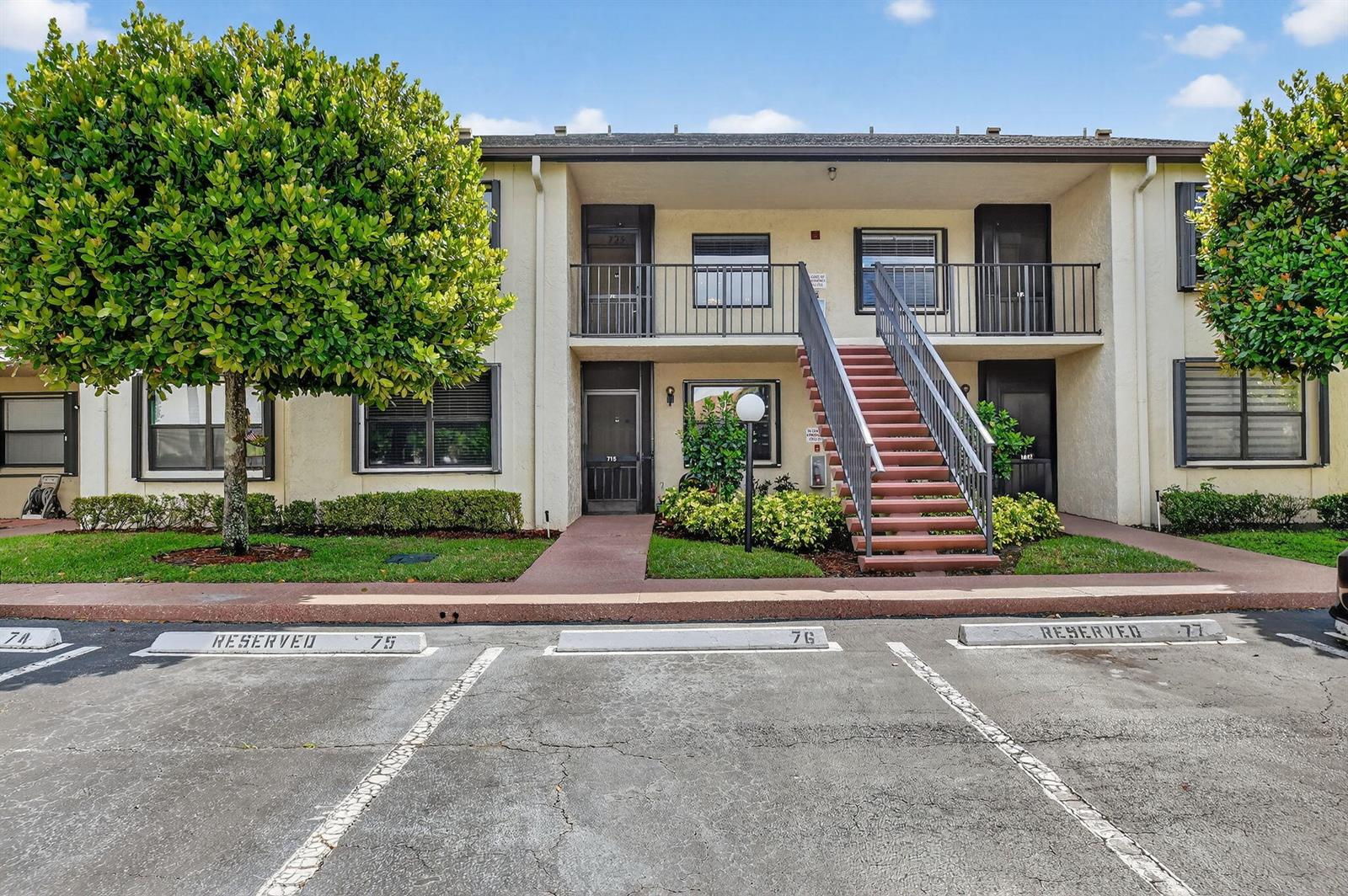 A two-story apartment building exterior features a central staircase, reserved parking spaces, and landscaping — 7855 Willow Spring Drive # 725, Lake Worth FL 33467, LAKE WORTH, FL