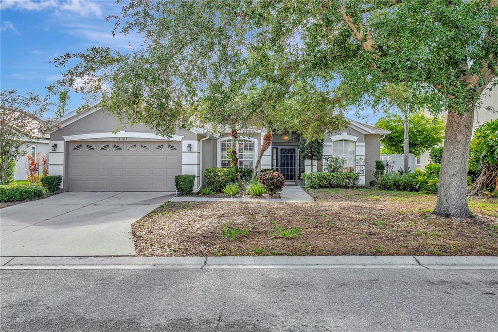 A single-story house with a beige garage, a front walkway, and a large shade tree — 4105 30TH LANE E, BRADENTON, FL