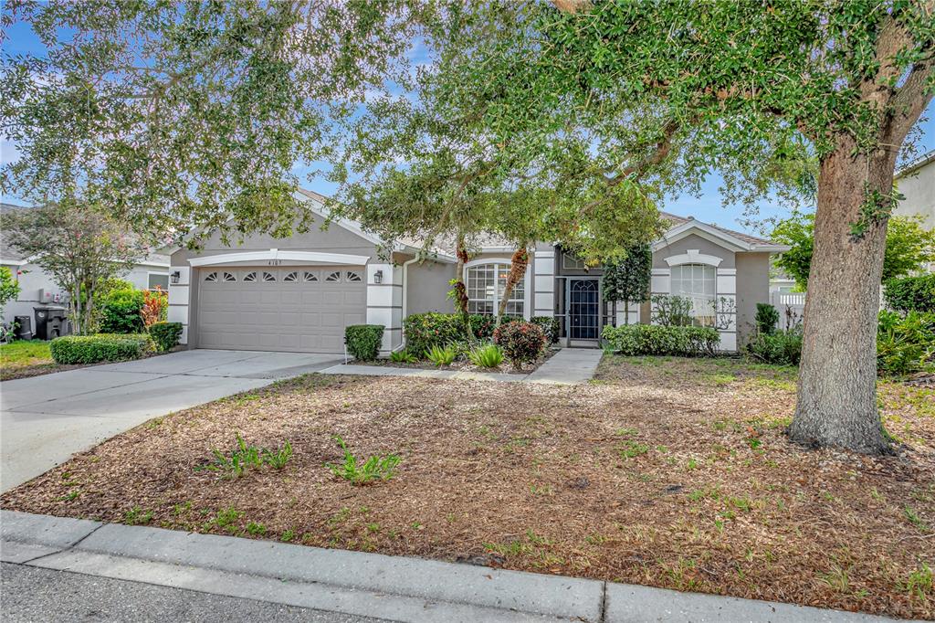 A single-story house with a beige exterior, a two-car garage, and a large front tree — 4105 30TH LANE E, BRADENTON, FL