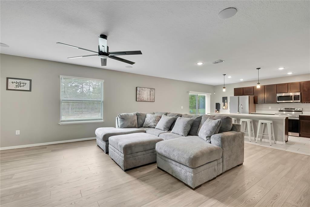 A living room with light wood floors, a large gray sectional, and an open kitchen — 16125 MAGPIE ROAD, WEEKI WACHEE, FL