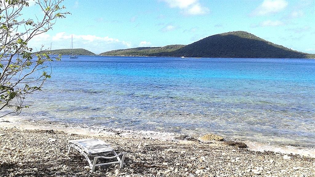 A lounge chair sits on a rocky beach overlooking a bay with distant islands — End of Road CAM PLAYA TAMARINDO, CULEBRA, PR