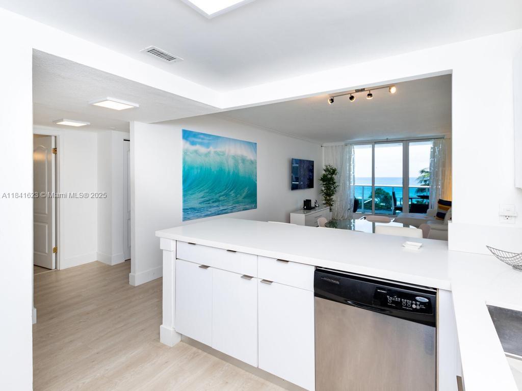 A white kitchen peninsula with a stainless steel dishwasher overlooks a living area with ocean views — 2301 Collins Ave # 625, Miami Beach FL 33139, MIAMI BEACH, FL