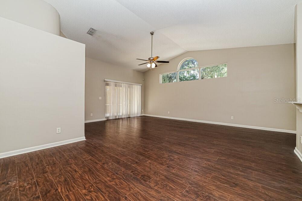 An empty living room features vaulted ceilings, a ceiling fan, and dark wood-look flooring — 4022 FONTANA PLACE, VALRICO, FL