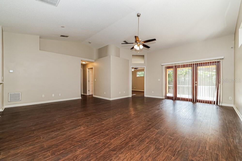 A living room with vaulted ceilings, dark wood-look flooring, and sliding glass patio doors — 4022 FONTANA PLACE, VALRICO, FL