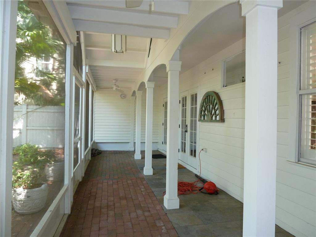 A covered porch with brick and stone flooring, white columns, and screened-in walls — 3302 W VILLA ROSA STREET, TAMPA, FL