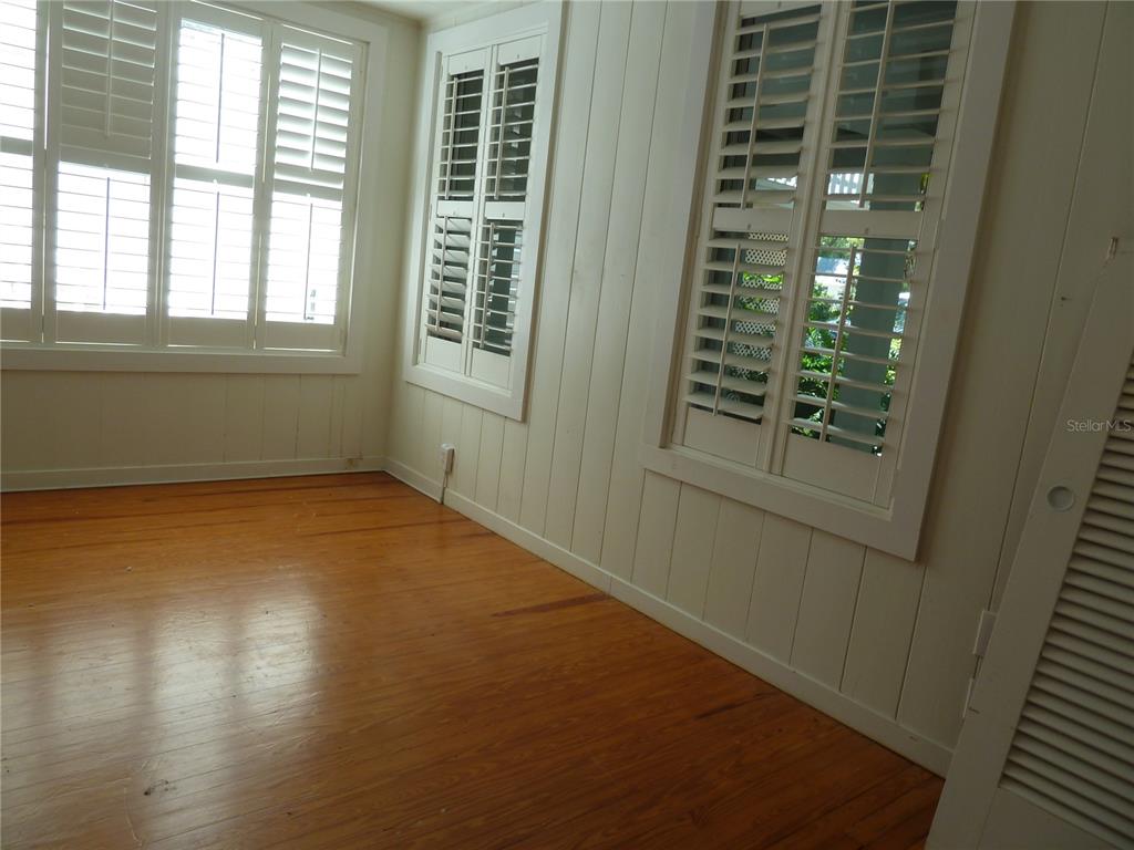 An empty room with hardwood floors, white vertical paneled walls, and white plantation shutters — 3302 W VILLA ROSA STREET, TAMPA, FL