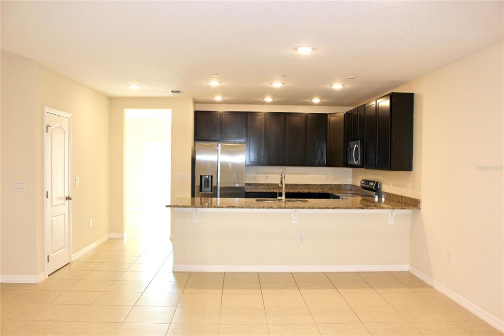 A kitchen features dark wood cabinets, granite countertops, a breakfast bar, and tile flooring — 4723 CORAL CASTLE DRIVE, KISSIMMEE, FL