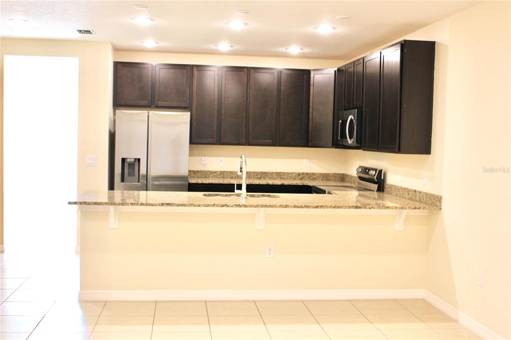 A kitchen with dark wood cabinets, granite countertops, and stainless steel appliances — 4723 CORAL CASTLE DRIVE, KISSIMMEE, FL