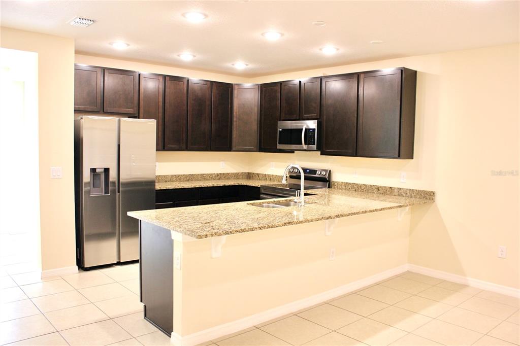 A kitchen features dark wood cabinets, granite countertops, stainless steel appliances, and tile flooring — 4723 CORAL CASTLE DRIVE, KISSIMMEE, FL