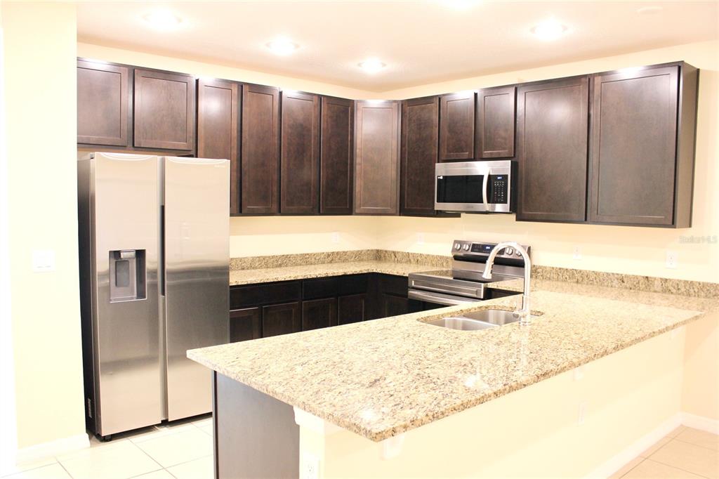 A kitchen features dark wood cabinets, granite countertops, and stainless steel appliances — 4723 CORAL CASTLE DRIVE, KISSIMMEE, FL