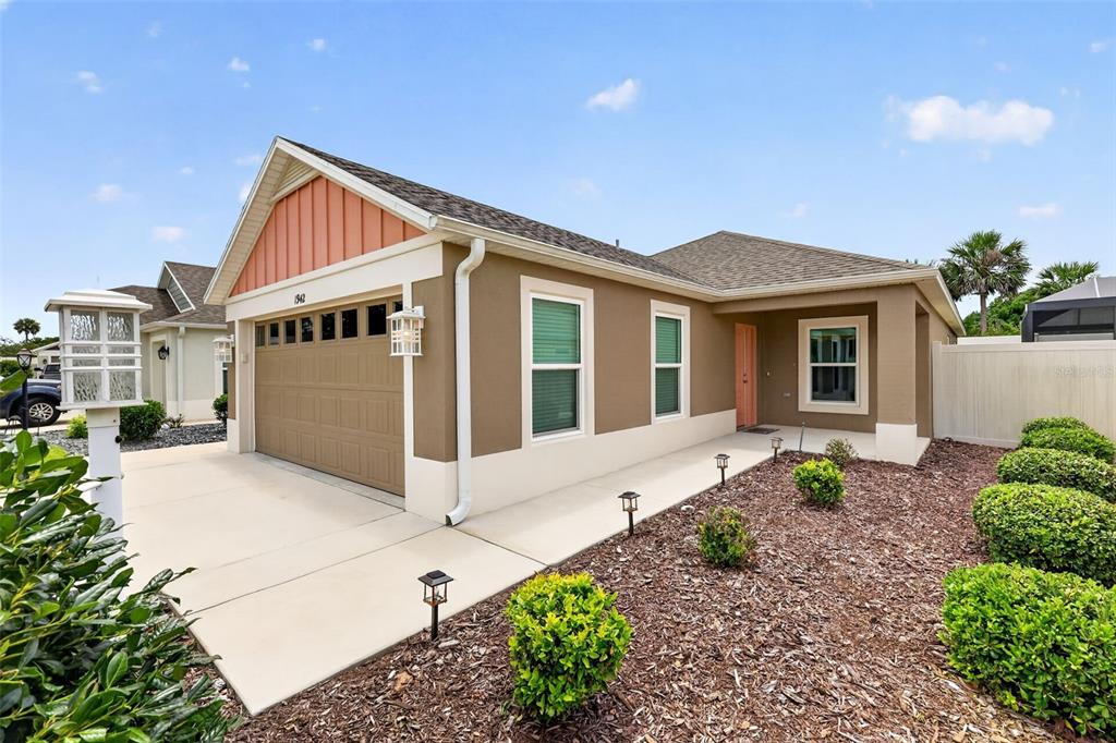 A single-story house with a tan exterior, a two-car garage, and a landscaped front yard — 1942 DETWILER LANE, THE VILLAGES, FL