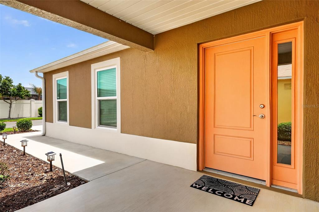 A covered porch features a bright orange front door with a matching side light window — 1942 DETWILER LANE, THE VILLAGES, FL