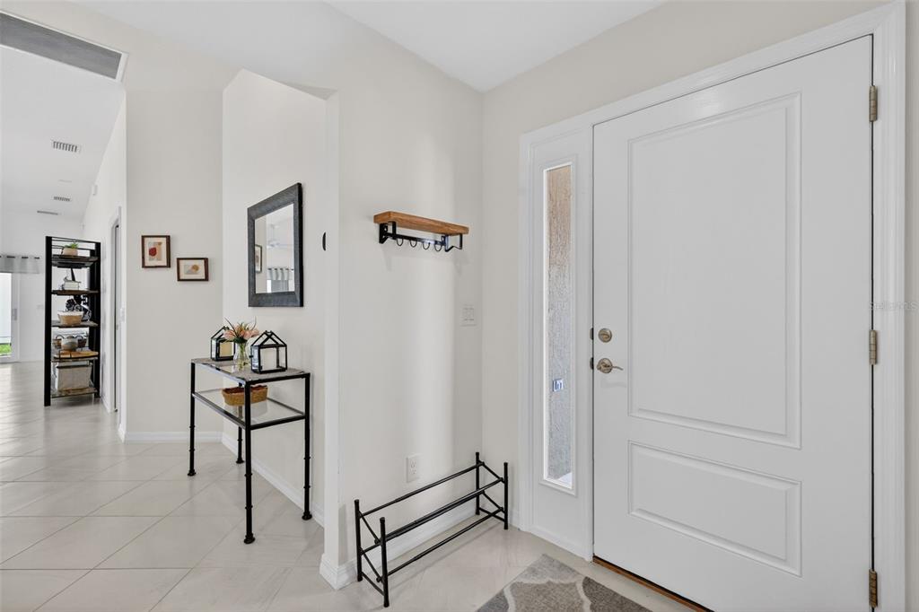 An entryway features a white front door, a glass console table, and a shoe rack — 1942 DETWILER LANE, THE VILLAGES, FL