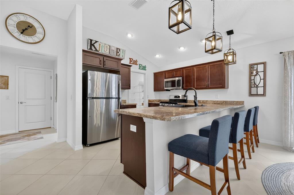 A kitchen features dark wood cabinets, granite countertops, stainless steel appliances, and three bar stools — 1942 DETWILER LANE, THE VILLAGES, FL