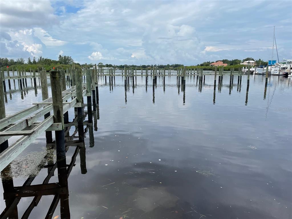 A wooden dock extends into a calm waterway with numerous pilings and distant boats — 507 ANCLOTE ROAD, TARPON SPRINGS, FL