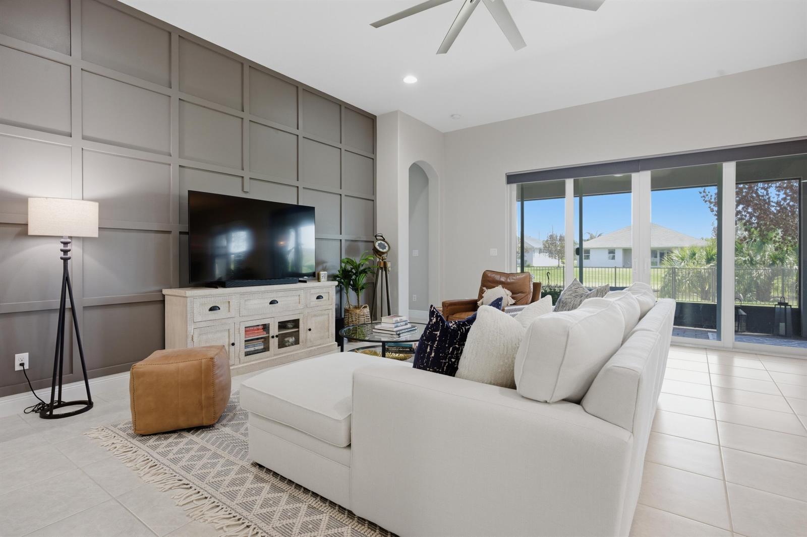 A living room features a paneled accent wall, a white sectional sofa, and sliding glass doors — 1650 Segovia Circle, Vero Beach FL 32966, VERO BEACH, FL