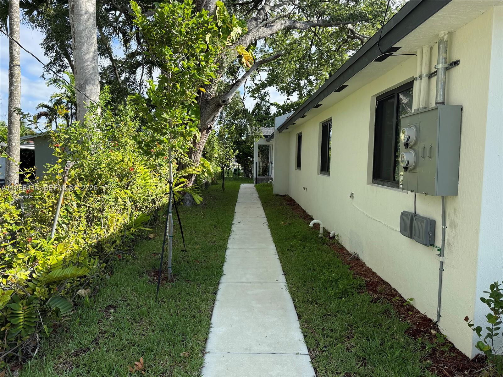 A concrete walkway runs along the side of a light yellow house with exterior electrical equipment — 210 SW 3rd St, Florida City FL 33034, FLORIDA CITY, FL