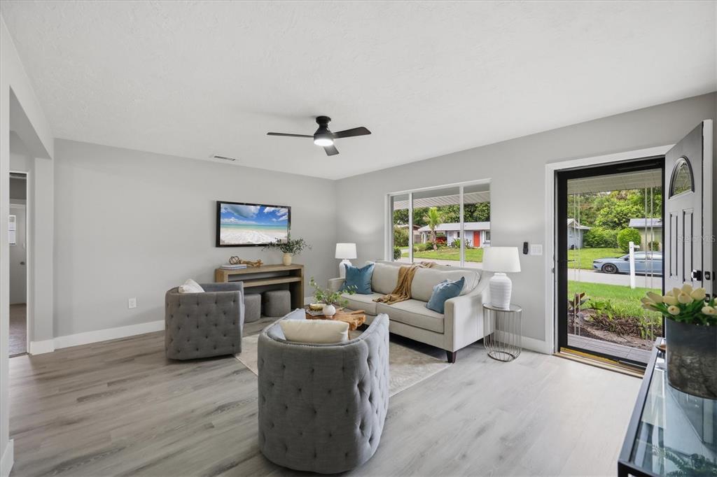 A living room features light gray walls, wood-look flooring, a sofa, two armchairs, and a ceiling fan — 4219 DEERFIELD DRIVE, SARASOTA, FL