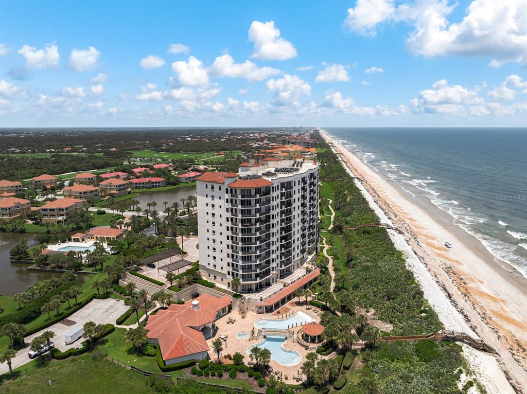 An aerial view shows a tall residential building next to a beach and ocean — 85 AVENUE DE LA MER UNIT 502, PALM COAST, FL