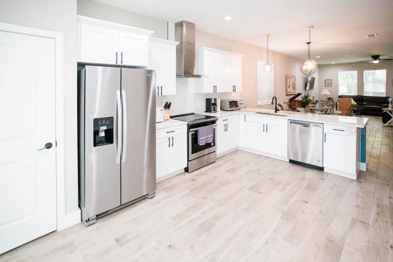 A modern kitchen features white cabinets, stainless steel appliances, and light wood-look tile flooring — 705 E ELM STREET, TAMPA, FL