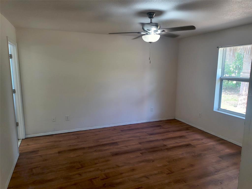 An empty room features wood-look flooring, white walls, a ceiling fan, and a window — 4 PROSPECT LANE UNIT A, PALM COAST, FL