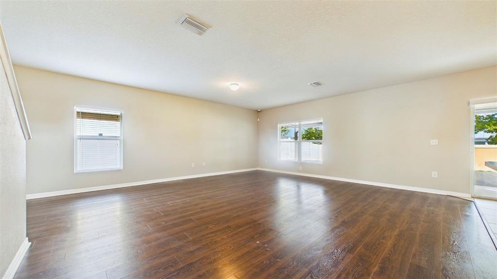 An empty living room features dark wood-look flooring, beige walls, and two windows — 14517 DUNROBIN DRIVE, WIMAUMA, FL