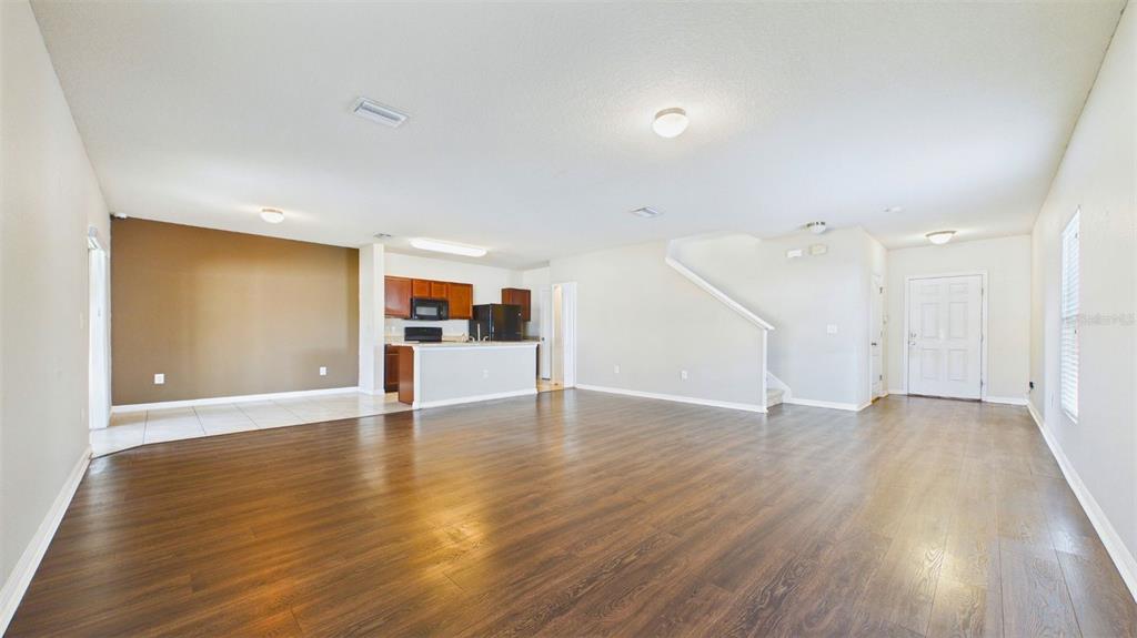 An open-concept living area features wood-look flooring, a kitchen with dark cabinets, and a staircase — 14517 DUNROBIN DRIVE, WIMAUMA, FL