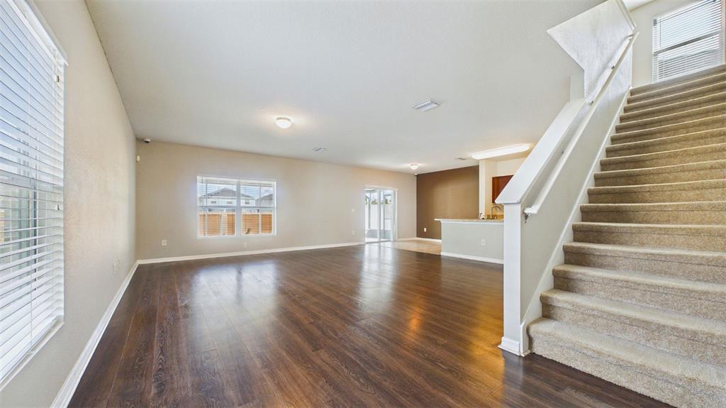 An open-concept living area features dark wood flooring, beige walls, and a carpeted staircase — 14517 DUNROBIN DRIVE, WIMAUMA, FL