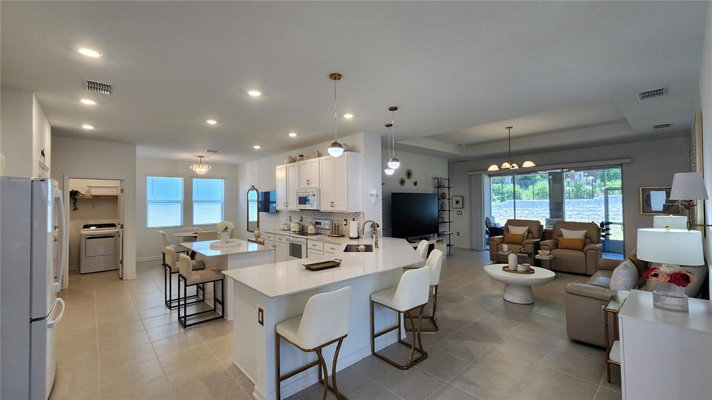 An open-concept kitchen and living area features white cabinetry, quartz countertops, and tile flooring — 2095 RIDER RAIN LANE, APOPKA, FL