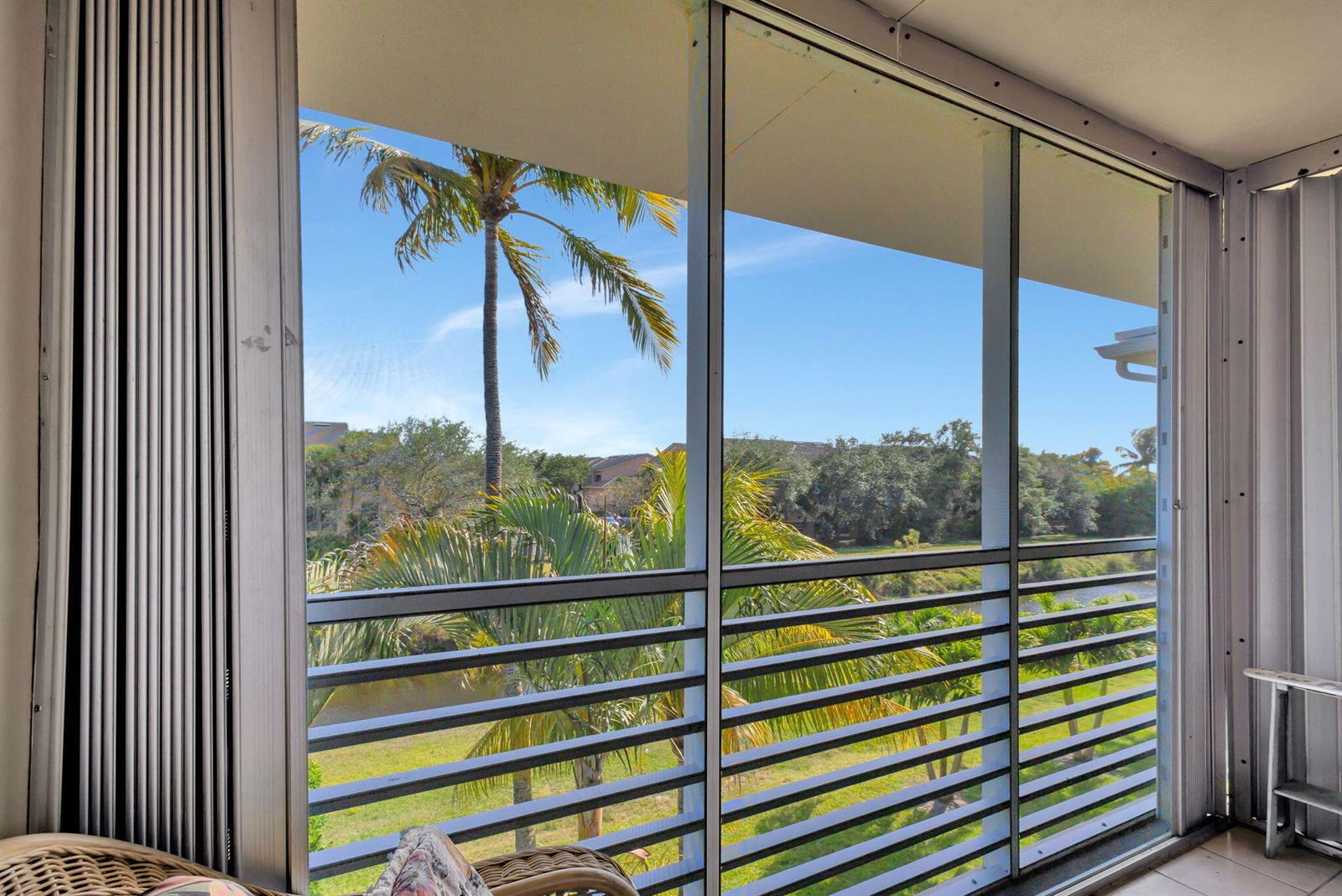 A screened-in balcony overlooks a grassy area, a small canal, and palm trees — 2812 Garden Drive S # 308, FL 33461, FL