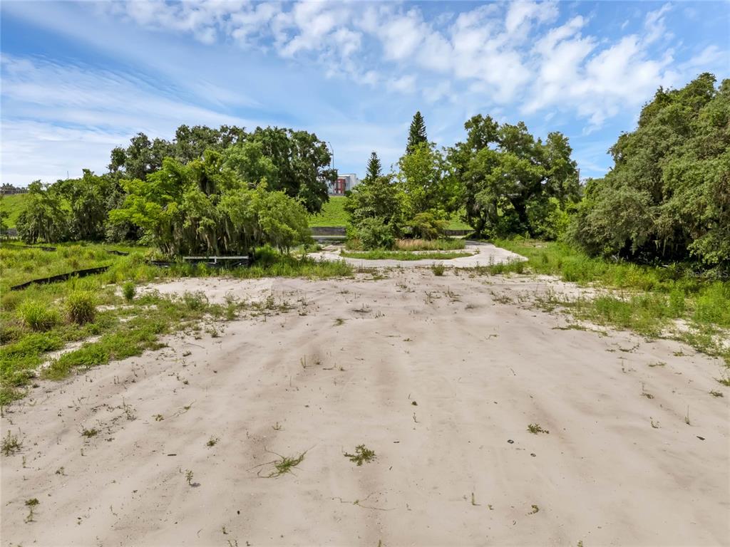 A sandy, undeveloped lot features scattered patches of grass and mature trees under a blue sky — 1250 N MAITLAND AVENUE, MAITLAND, FL