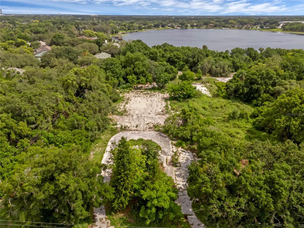 An aerial view shows a cleared, paved lot surrounded by dense trees near a lake — 1250 N MAITLAND AVENUE, MAITLAND, FL