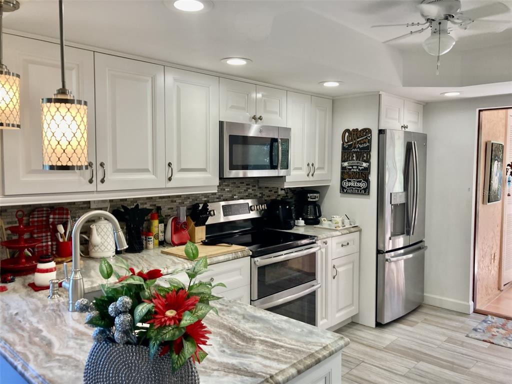 A kitchen features white cabinets, stainless steel appliances, and a marble-patterned countertop island — 6002 OAK CREEK LANE UNIT 1925, BRADENTON, FL