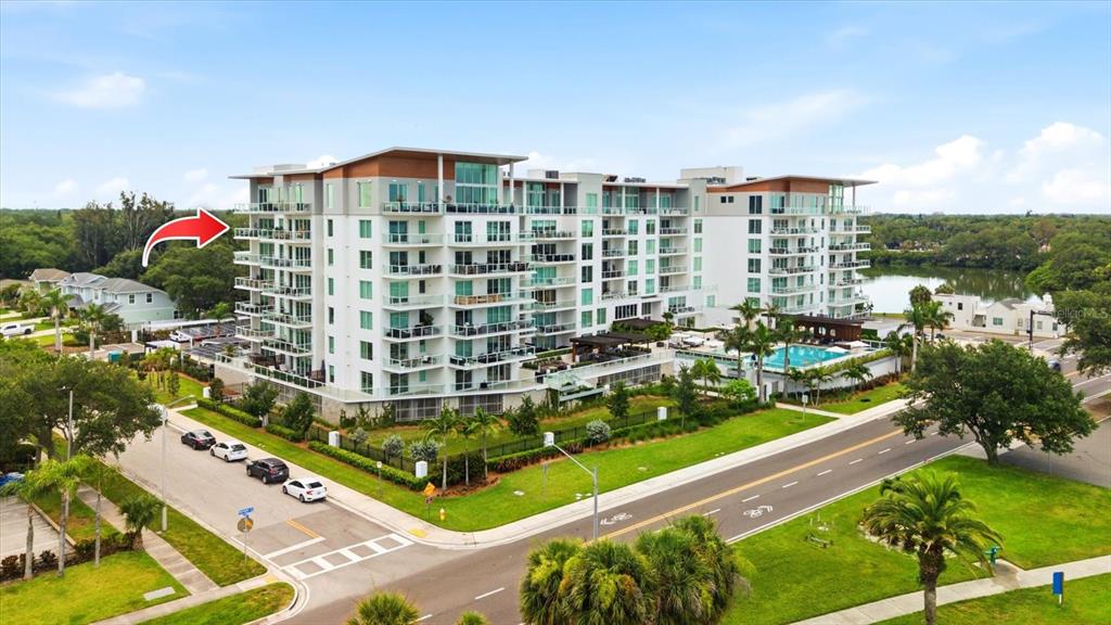 An aerial view of a modern multi-story apartment building with balconies and an outdoor pool — 1020 SUNSET POINT ROAD UNIT 601, CLEARWATER, FL