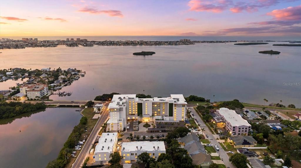 An aerial view shows a multi-story hotel complex situated along a bay at sunset — 1020 SUNSET POINT ROAD UNIT 601, CLEARWATER, FL