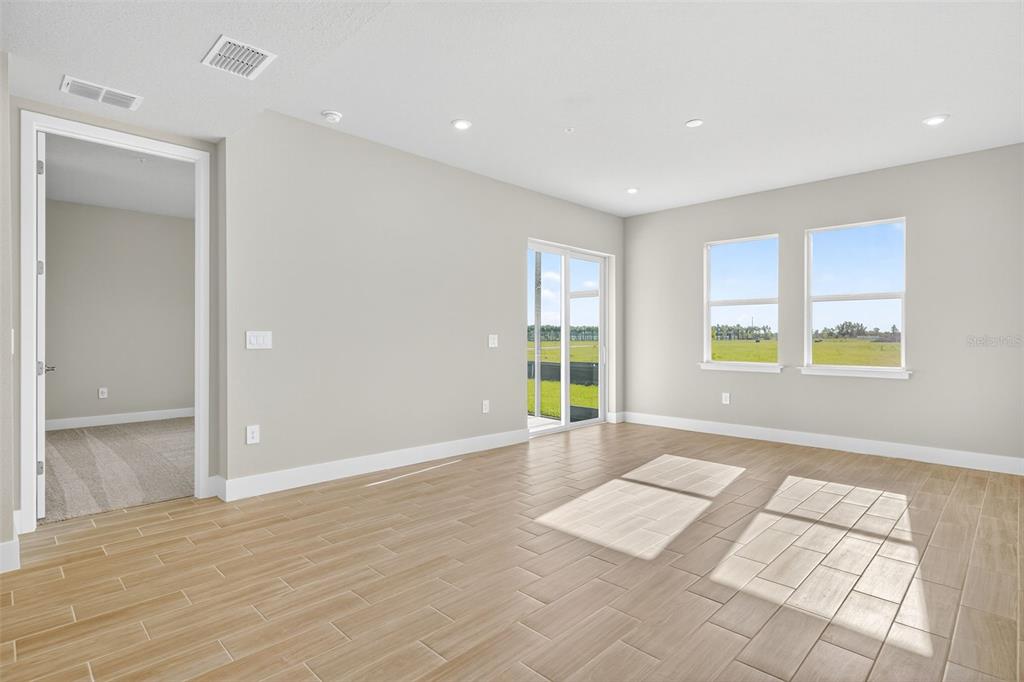 A bright, empty room features light-colored tile flooring, neutral walls, recessed lighting, and large windows — 17420 MOONFLOWER DRIVE UNIT 102, VENICE, FL