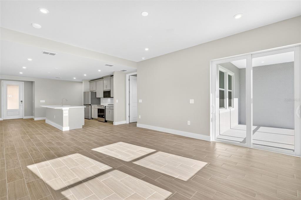 An open-concept living area features light-colored tile flooring, a kitchen with white cabinets, and sliding doors — 17420 MOONFLOWER DRIVE UNIT 102, VENICE, FL