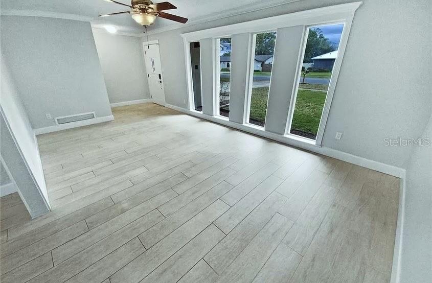 A bright room features light wood-look tile flooring, a ceiling fan, and large floor-to-ceiling windows — 7641 VILLAGE GREEN DRIVE, WINTER PARK, FL