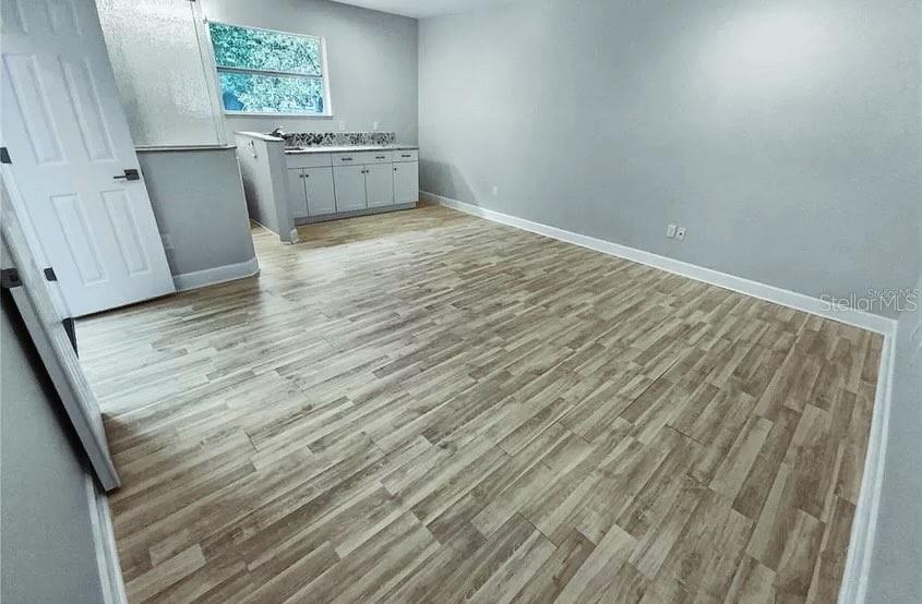 A room with light wood-look flooring, gray walls, and a small kitchenette area — 7641 VILLAGE GREEN DRIVE, WINTER PARK, FL