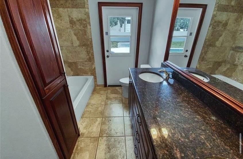 A bathroom features a dark wood vanity with a granite countertop, a bathtub, and a door — 7641 VILLAGE GREEN DRIVE, WINTER PARK, FL