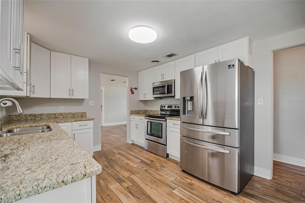 A kitchen features white cabinets, granite countertops, stainless steel appliances, and wood-look flooring — 2201 CAMELLIA DRIVE, LONGWOOD, FL