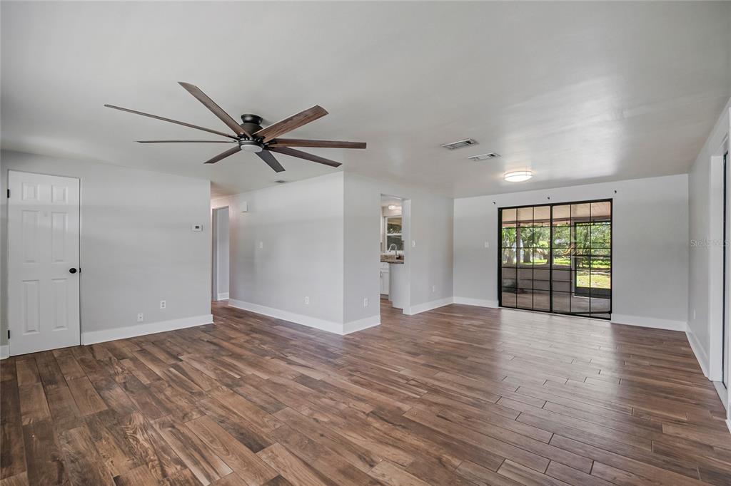 An open-concept living room features wood-look tile flooring, a ceiling fan, and sliding glass doors — 2201 CAMELLIA DRIVE, LONGWOOD, FL